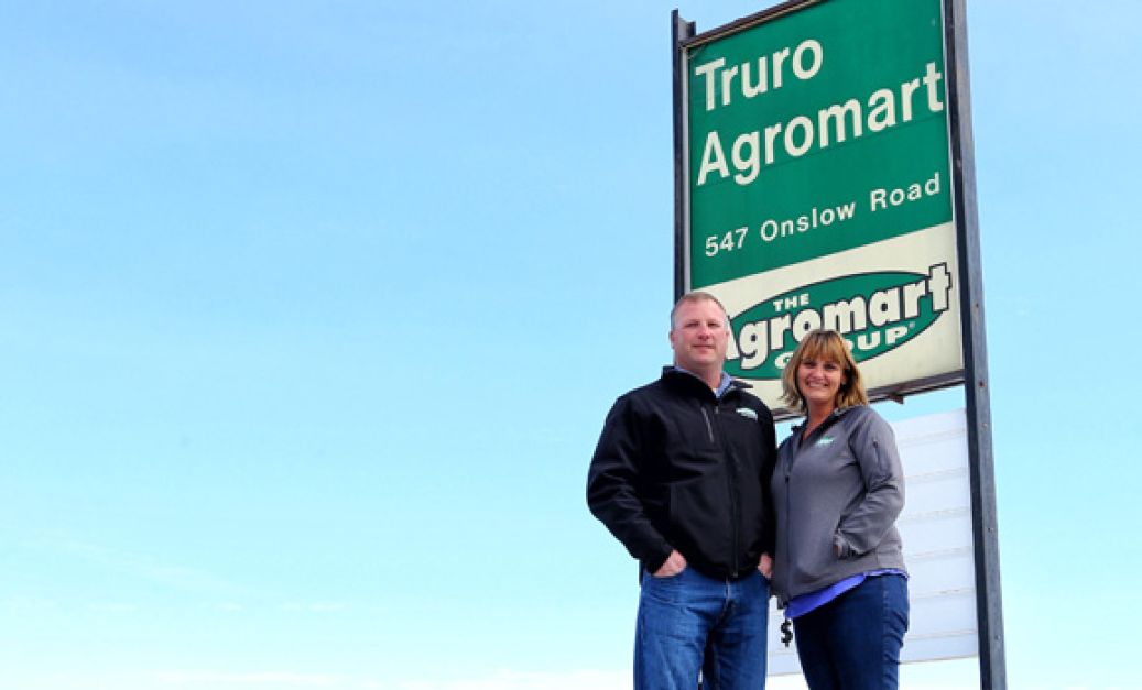Owners of Truro Agromart with sign in the background and blue skies